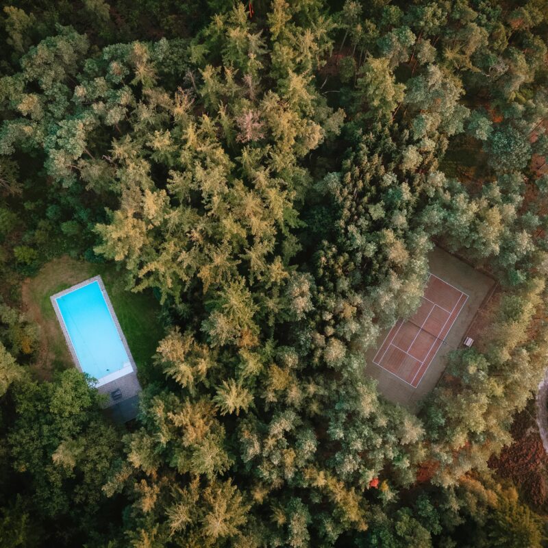 Een bovenaanzicht van het buitenzwembad en de tennisbaan die zich op Landgoed Noorderheide bevinden