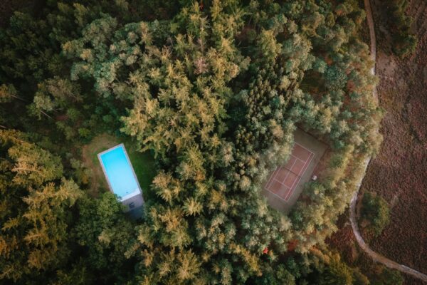 Een bovenaanzicht van het buitenzwembad en de tennisbaan die zich op Landgoed Noorderheide bevinden