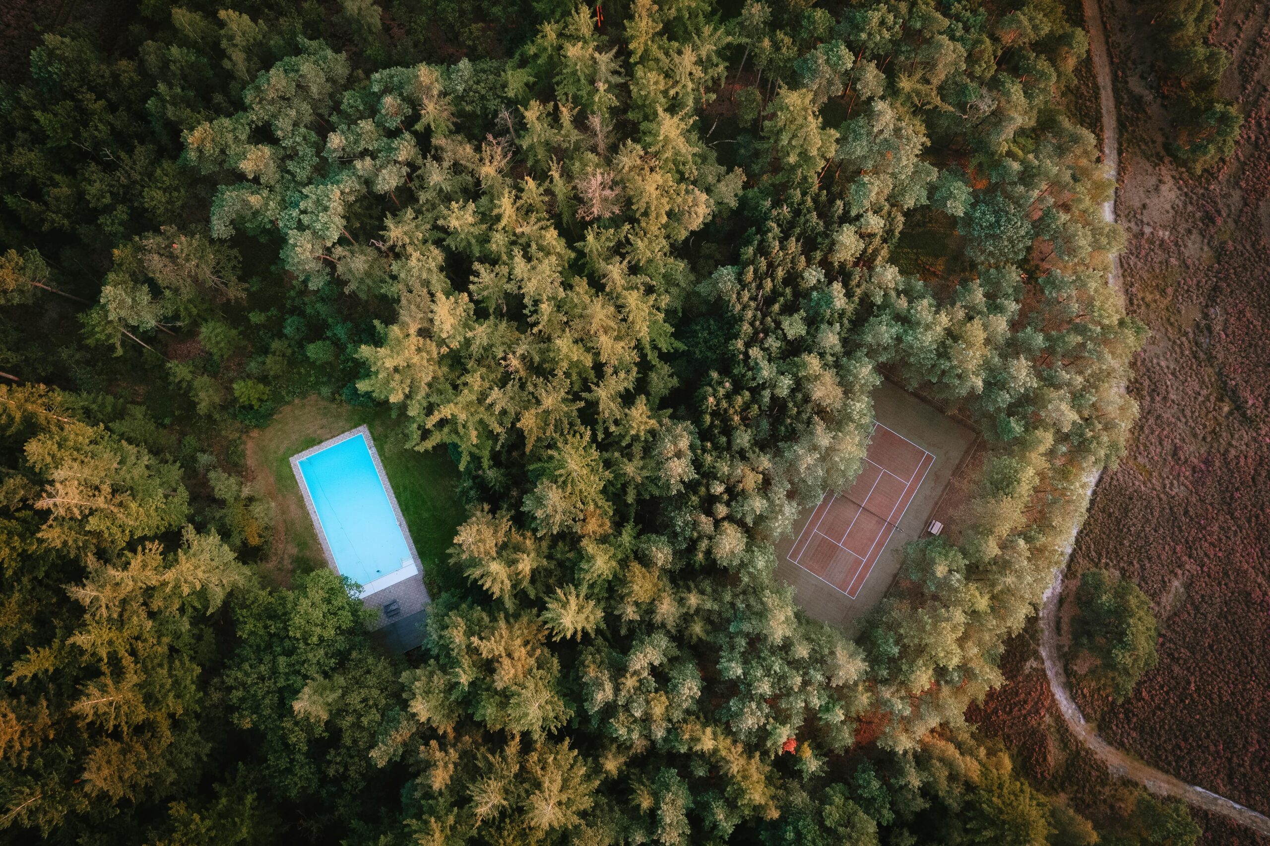 Een bovenaanzicht van het buitenzwembad en de tennisbaan die zich op Landgoed Noorderheide bevinden