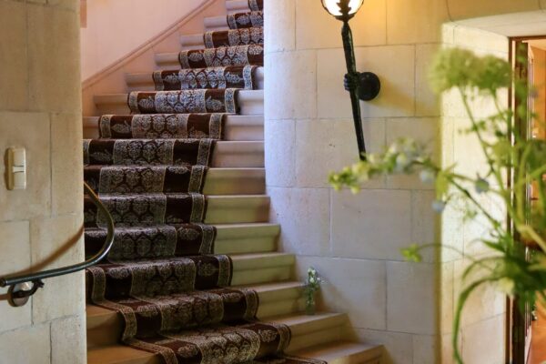 De hal met een mooie stenen trap en daarop gedrapeerd een fraai tapijt