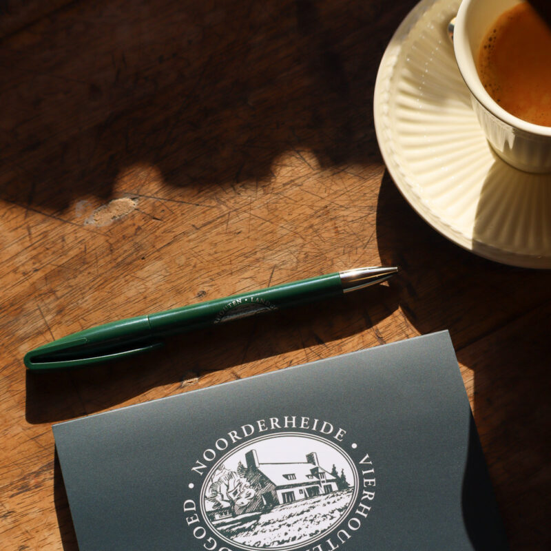Een notitieblok met het logo van Landgoed Noorderheide naast een kop koffie